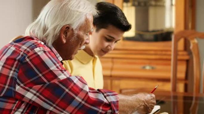 高年级男子在家帮助孙子做学校作业