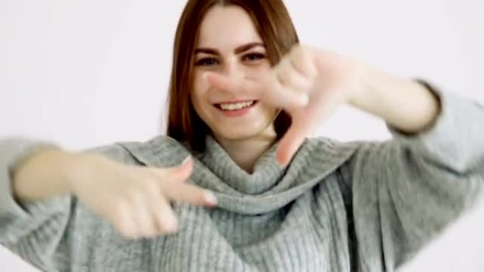 穿着温暖毛衣的欧洲美女在白色墙壁上摆姿势。在虚构的相机上大笑并拍照。