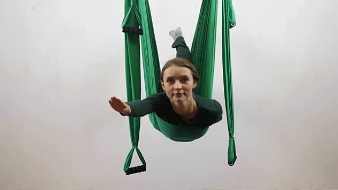 年轻的白人妇女在室内工作室的吊床上做反重力飞行瑜伽练习。空中飞行健身教练锻炼。超人姿势、冥想、和谐与