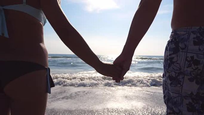恋爱中的年轻夫妇站在海边，欣赏美丽的景色。男性和女性的手臂在海滩上互相安慰和抚摸。暑假或假期。关闭后