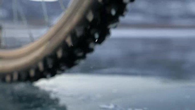 轮胎视图。拍摄180fps。女人在冰上骑自行车。冰冻的贝加尔湖的冰。自行车上的轮胎上覆盖着特殊的钉子