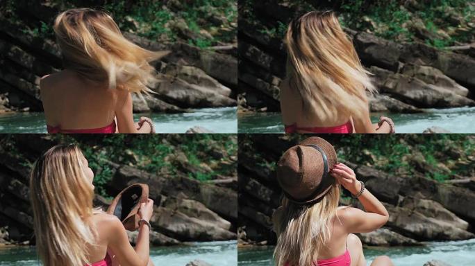 年轻女子坐在瑞士山河岸边的岩石上。脱下帽子，张开长发。自由和纯洁的概念，快乐。卸掉枷锁。慢动作。特写
