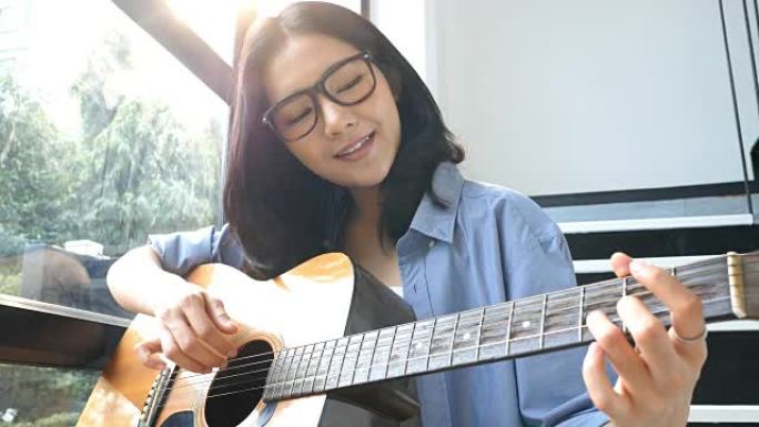迷人的亚洲女人在家里微笑着弹吉他。