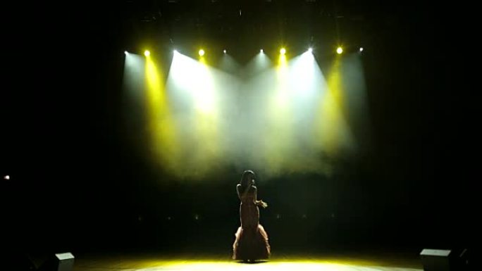 美丽的女孩在发光的舞台上唱歌。