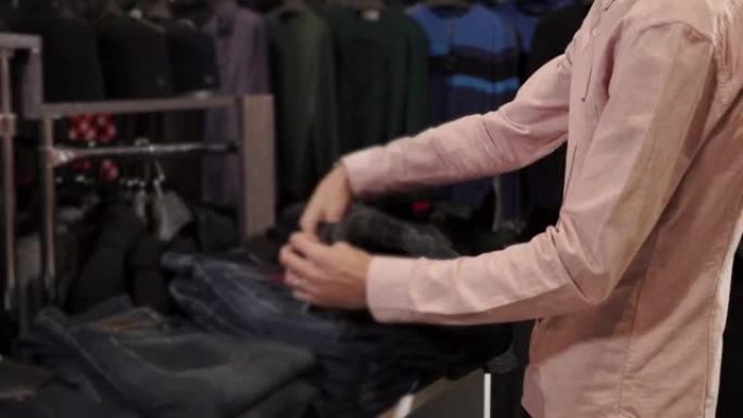 年轻人正在服装店检查牛仔长裤的价格，触摸商品