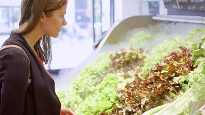 年轻女子在杂货店购物。站在蔬菜部门选择新鲜的绿色沙拉