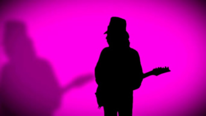戴着阴影的帽子的酷摇滚吉他手正在粉红色背景上弹奏电吉他。