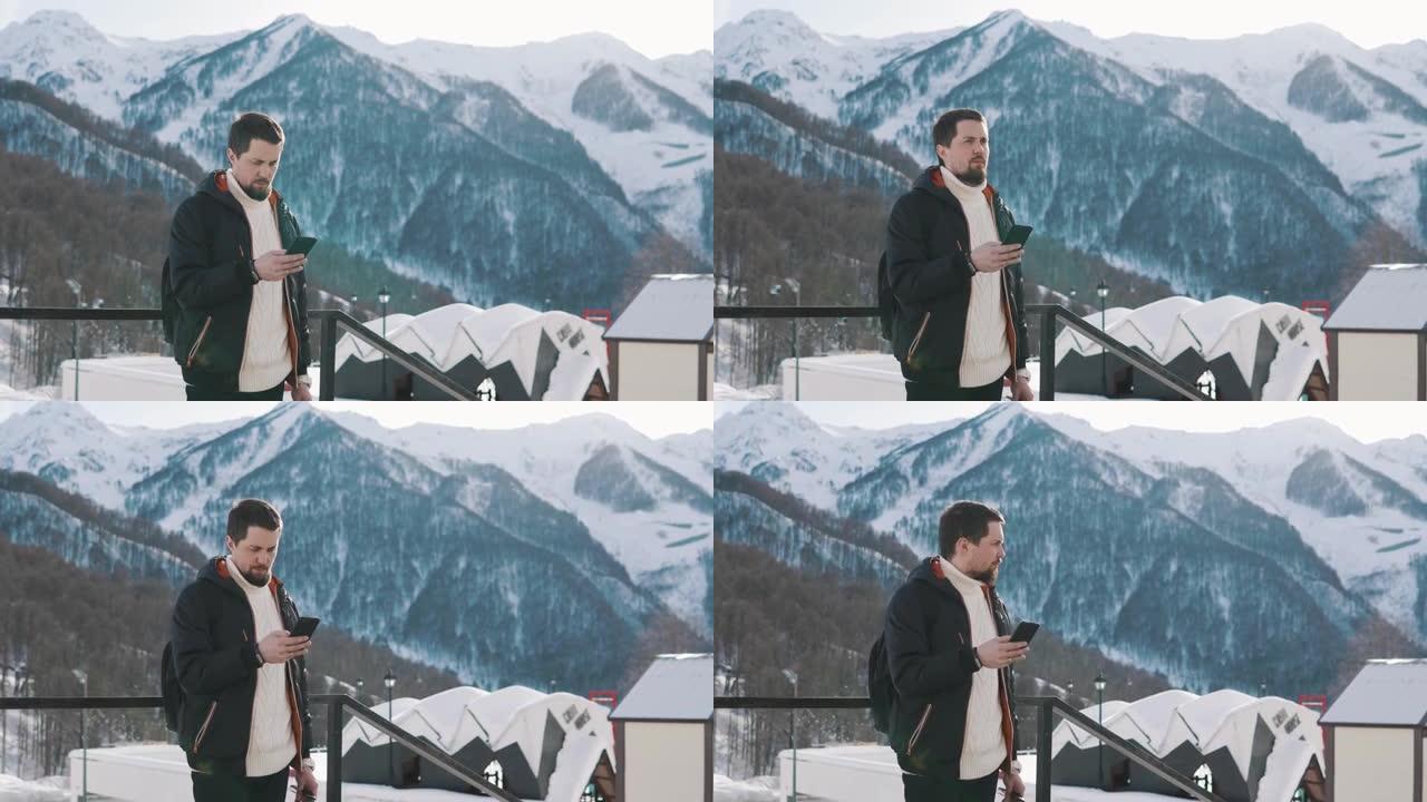 男子使用手机发送信息，站在山上的滑雪基地户外