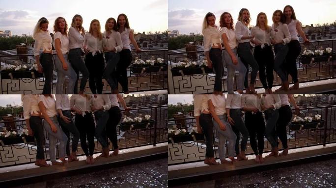 六个高加索女孩站在阳台上，对着镜头摆姿势。休闲服。女孩穿着牛仔裤的腿特写。旧城背景