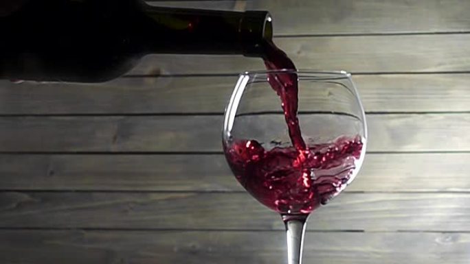 将红酒倒入木制背景的玻璃杯中。慢动作