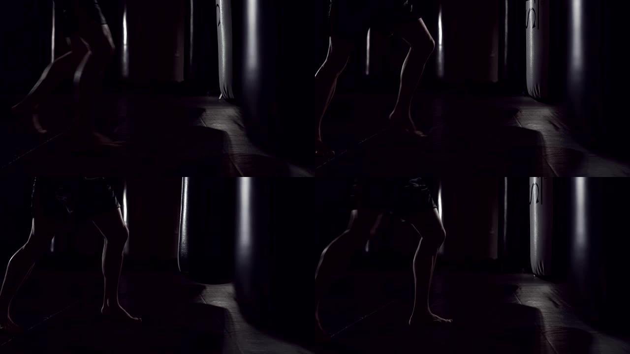 沙袋旁的脚影。慢镜头序列。一个强壮的运动员进入沙袋。在跆拳道里的男人在健身房里训练手提包。慢动作