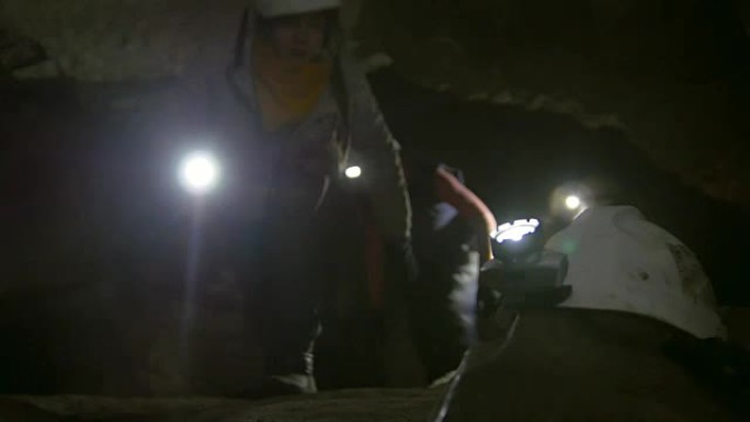 洞穴学家面前的手电筒头盔探索了黑暗的狭窄洞穴