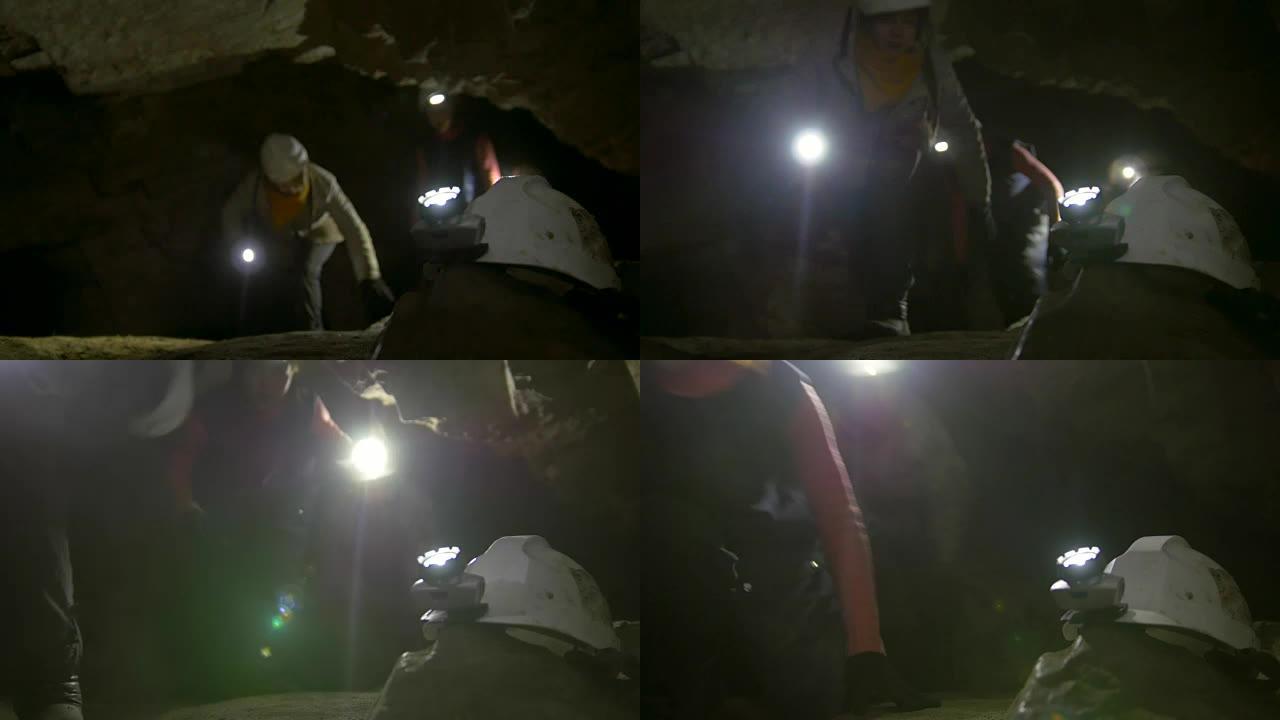 洞穴学家面前的手电筒头盔探索了黑暗的狭窄洞穴