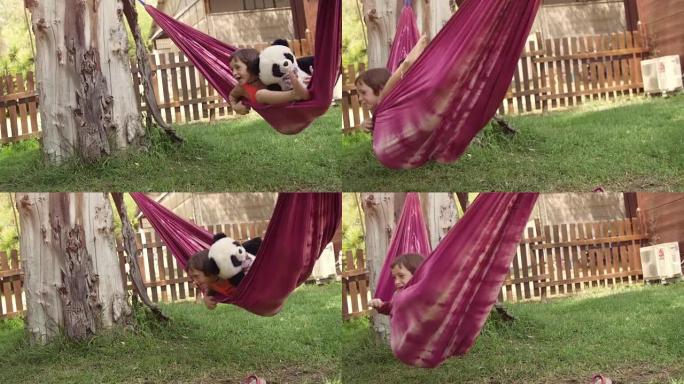 夏令营中年轻快乐的小女孩躺在五颜六色的吊床上放松地在外面玩绿色草地上的毛绒熊猫娃娃儿童慢动作