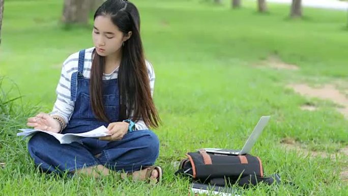 微笑着美丽的亚洲女孩读书，夏天在公园的树上工作，放松一下