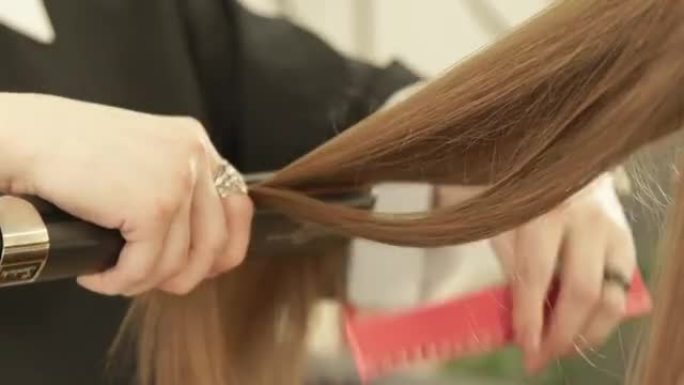 发型师在美容院使用发钳和梳子来拉直时尚模特。在美发沙龙的女性发型设计中，近距离美发师拉直长发