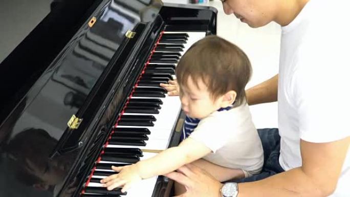 从上方看: 婴儿坐在父亲的膝盖上，尝试弹钢琴