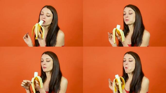 有趣的年轻饥饿的女人在明亮的橙色背景上吃香蕉。热带水果。节食概念。