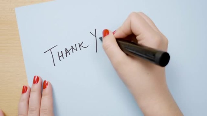 女人用红色指甲油的手在蓝色纸上写上黑色记号笔谢谢