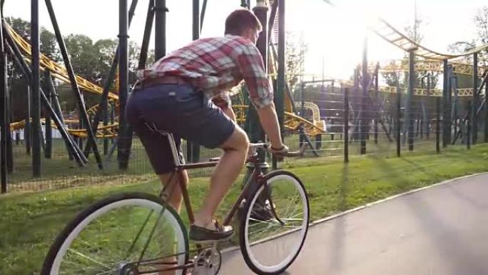 年轻英俊的男人在游乐园骑老式自行车。运动男在户外骑自行车。背景阳光普照。健康积极的生活方式。特写侧视