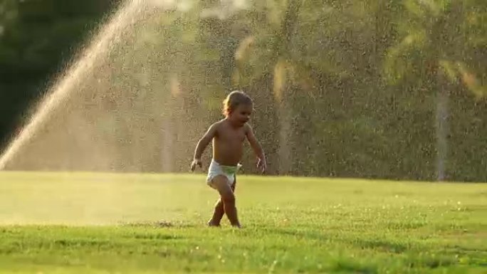 婴儿在黄金时段日落时分洒水奔跑。婴儿婴儿3岁男孩在暑假期间以4k分辨率在绿色田野中奔跑