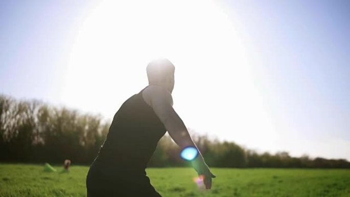 一个穿着黑色t恤的男人正在绿色的草地上做运动。用一只手举起重量，并将其保持在顶部。背面视图