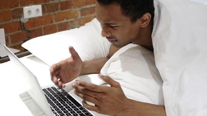 沮丧的非洲男子对笔记本电脑的损失做出反应，躺在肚子上