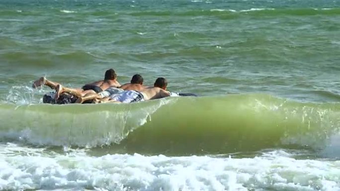 男人在充气床垫上在海里游泳。他们在笑。床垫在海浪上折腾。慢动作。
