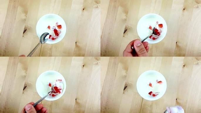 男人用勺子在木桌上慢动作吃健康的草莓和白色酸奶，这是健康食品的概念