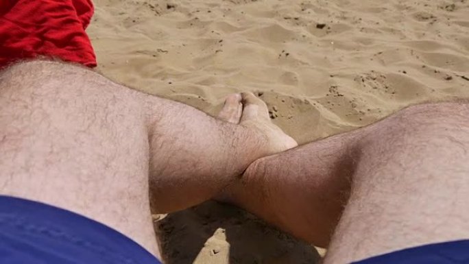 一个男人躺在沙滩上的腿。年轻人在度假胜地的躺椅上放松。