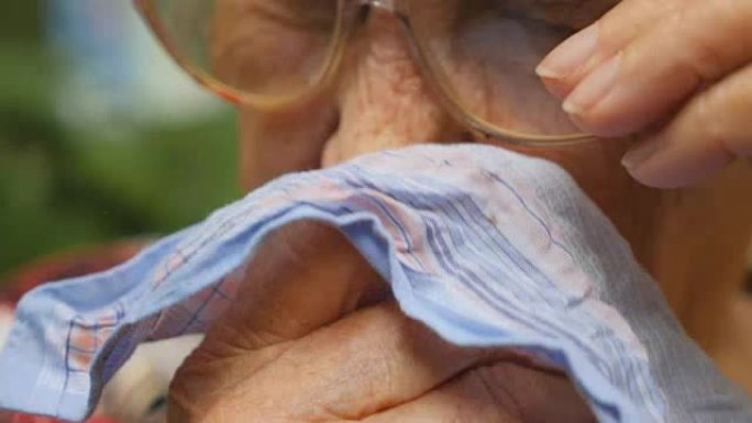 戴眼镜的祖母在户外把鼻子吹到手帕上。一个生病的老妇人的肖像。关闭慢动作