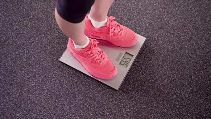 女孩在电子秤上测量她的体重。数字天平上穿着粉色运动鞋的苗条女性腿