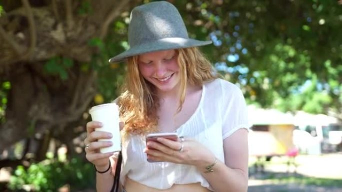 Woman walking in the park drinking coffee and usin