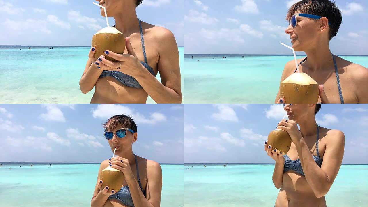 在热带岛屿海滩上喝椰子汁的成年妇女
