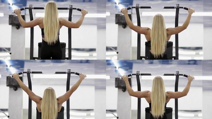 强壮的女性健美运动员，金发，肌肉发达的手臂在健身房的单杠上拉起。背面镜头