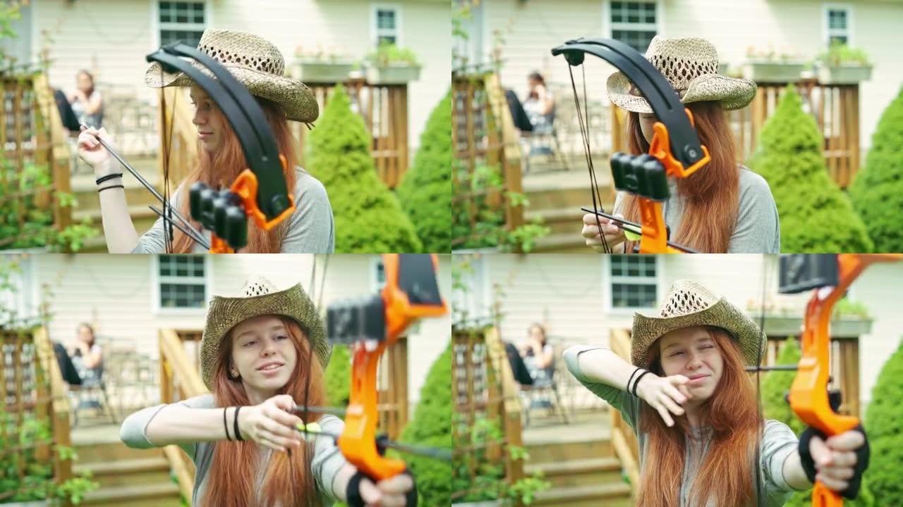 十几岁的女孩戴着帽子在后院练习射箭，她的妹妹在门廊上看着。