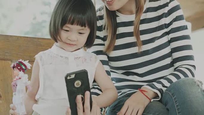 泰国女婴在妈妈旁边用智能手机和爸爸说话时玩洋娃娃 -- 幸福家庭休闲活动
