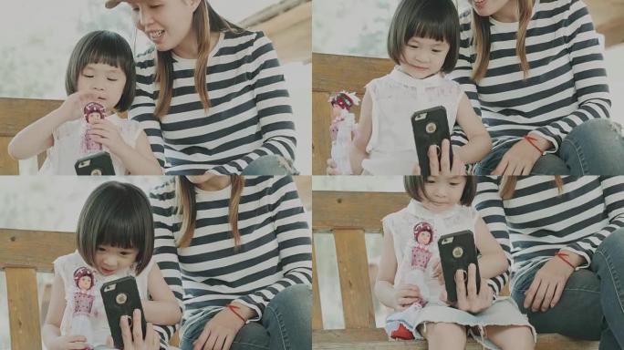 泰国女婴在妈妈旁边用智能手机和爸爸说话时玩洋娃娃 -- 幸福家庭休闲活动