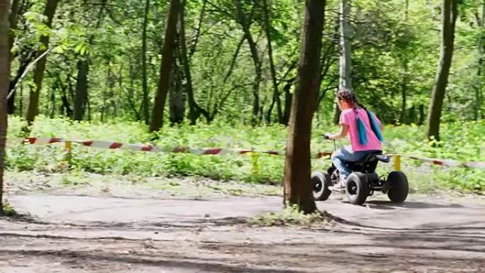 夏日在公共的pine city公园里，小女孩穿着鲜艳的粉红色t恤，配彩色辫子，骑着孩子的四轮摩托车，