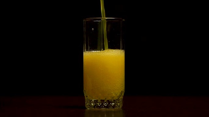 橙色苏打大玻璃，满溢的橙色苏打特写玻璃与气泡隔离在黑色背景。倒橙色饮料。慢动作。将碳酸橙汁倒入玻璃杯
