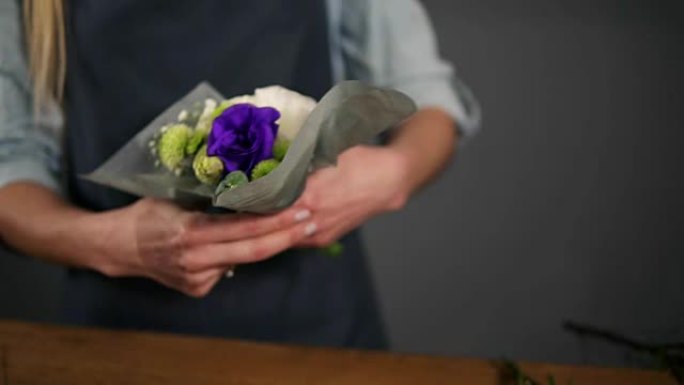 女性花店用装饰纸包裹一束花的手的特写视图。慢动作镜头