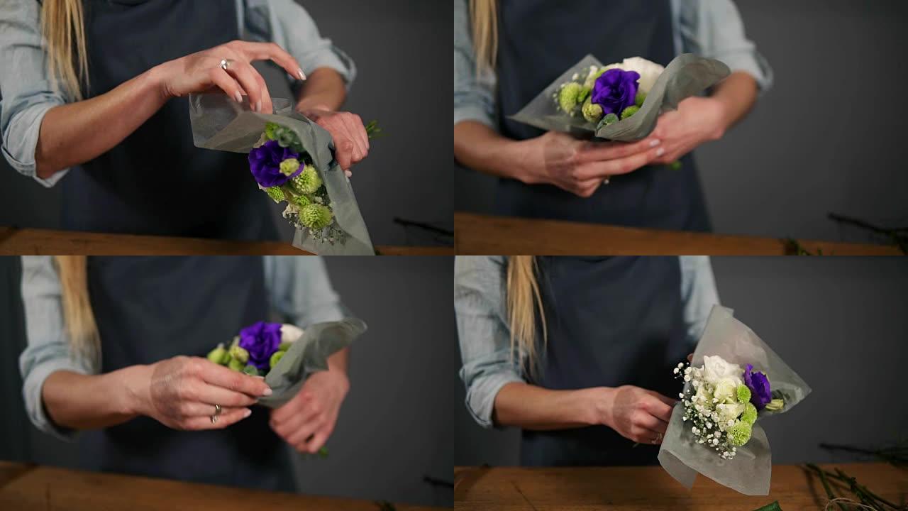 女性花店用装饰纸包裹一束花的手的特写视图。慢动作镜头
