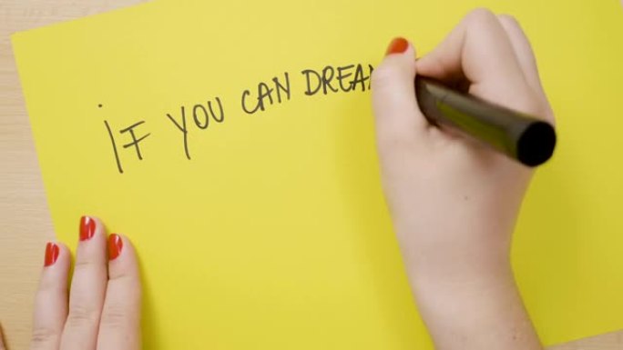 年轻女孩的手写作如果你能梦想它，你可以用黑色记号笔在黄纸上做激励性报价