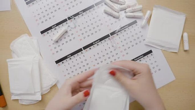 年轻的vlogger女性用红色修指甲将社交媒体影响者交给桌子上的日历上的卫生棉条和垫子