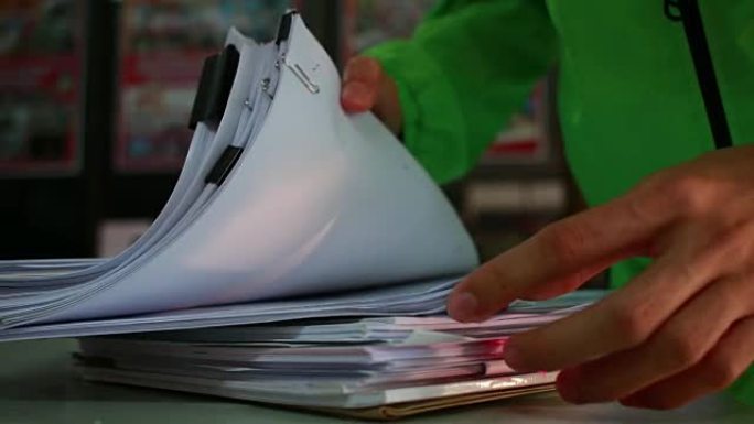 商人手在办公桌上搜索未完成的文档堆的纸质文件以获取报告文件，在桌子上用夹子将纸张堆成，文件被书写，绘