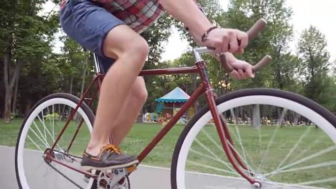无法辨认的年轻人骑着老式自行车。运动男在公园骑自行车。健康积极的生活方式。低角度视图特写慢动作侧视图