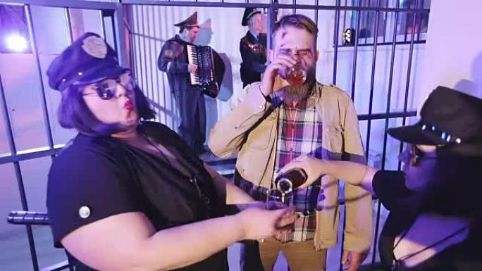 监狱牢房里的一个派对。一名身穿制服的女警察向一名留着胡须的流浪汉倒酒。