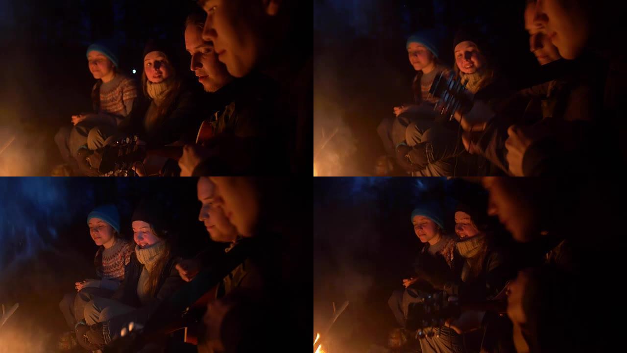 团体og朋友在夜林营火前向吉他唱歌