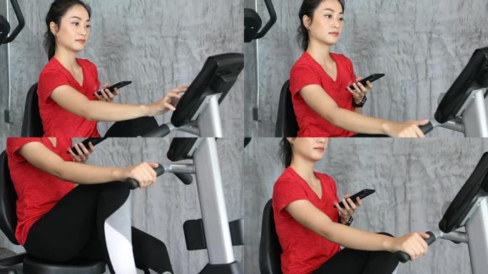 美女骑健身车骑自行车，在健身房使用智能手机