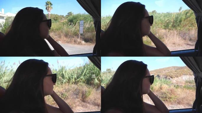 戴墨镜的女孩在旅途中看着窗外。年轻女子夏天乘公共汽车旅行，看着窗户。女游客乘坐汽车。度假或游览概念。